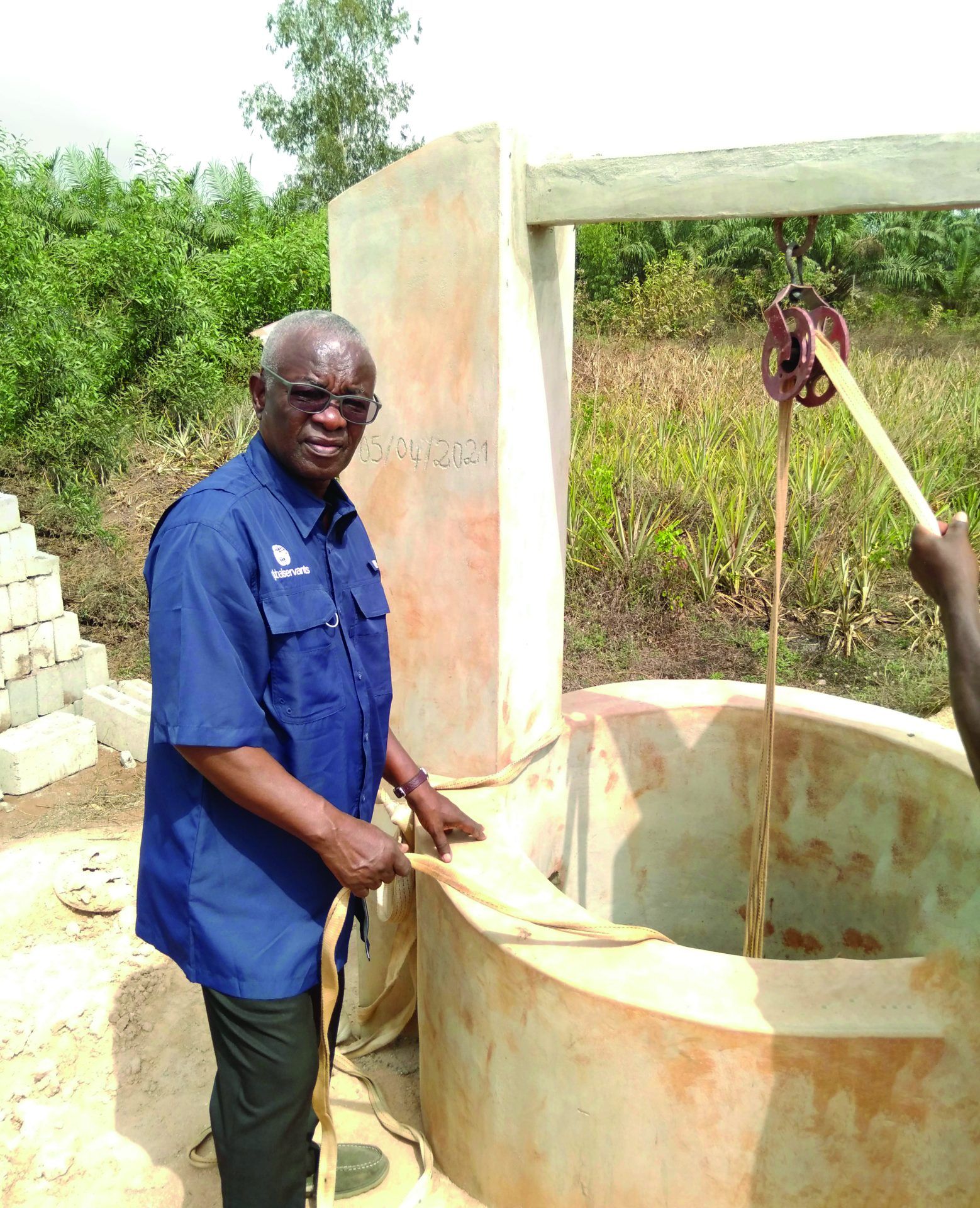 A man in a blue shirt is standing next to a well.