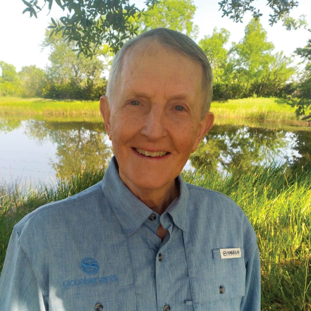 A man in a blue shirt is smiling in front of a lake