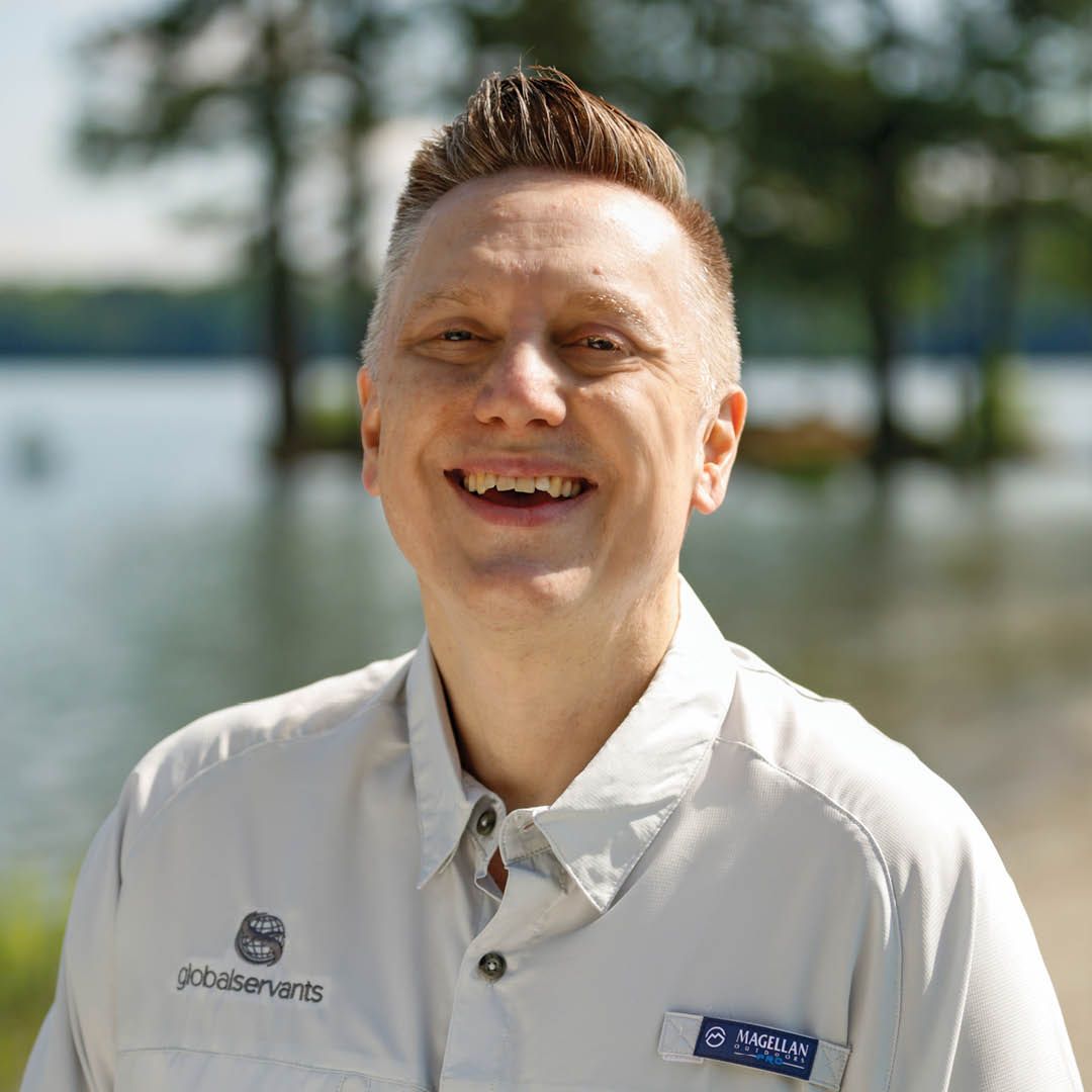 A man in a white shirt is smiling in front of a body of water.