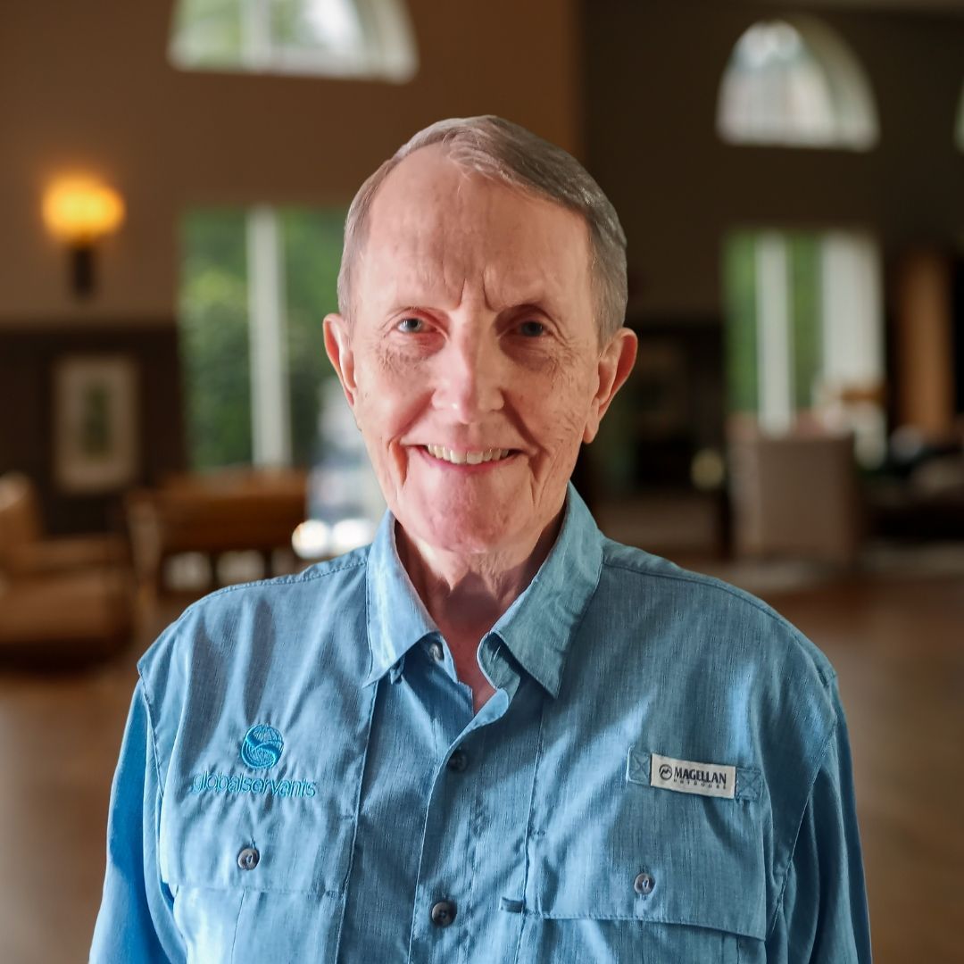 A man in a blue shirt is smiling in front of a lake
