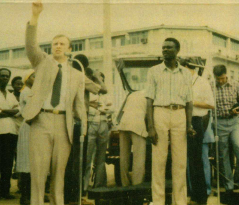 A man in a suit and tie raises his hand in the air