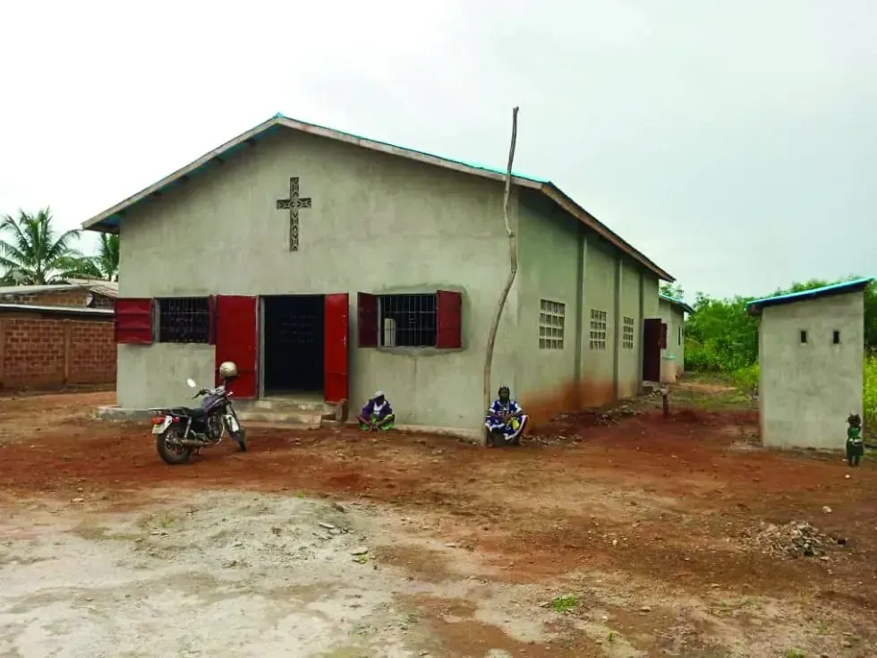 A motorcycle is parked in front of a church with a cross on the roof.