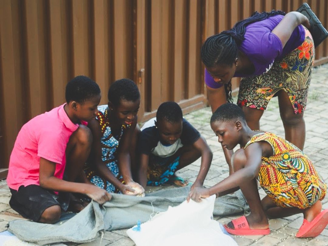 Children and an adult gather around fabric outdoors, looking down.