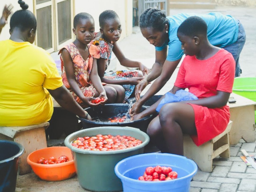 People wash tomatoes in a large tub. Several buckets of tomatoes surround them.