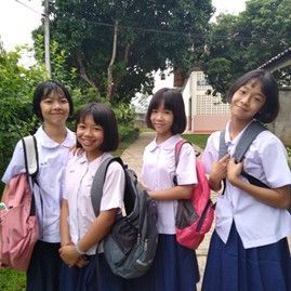 A group of young girls wearing school uniforms and backpacks are standing next to each other.