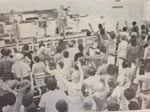 A large group of people are standing on a boat with their arms in the air.