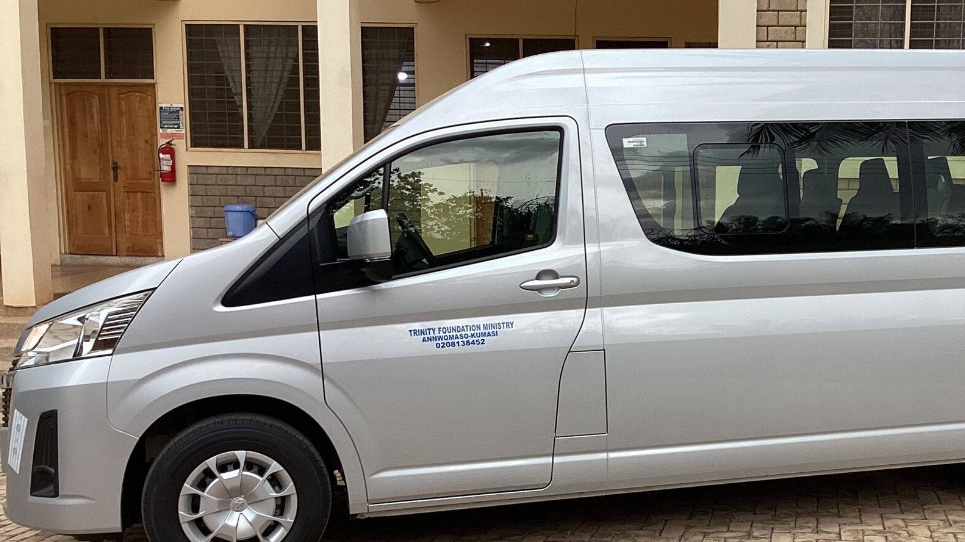 Silver passenger van parked outside a building with windows and a wooden door.