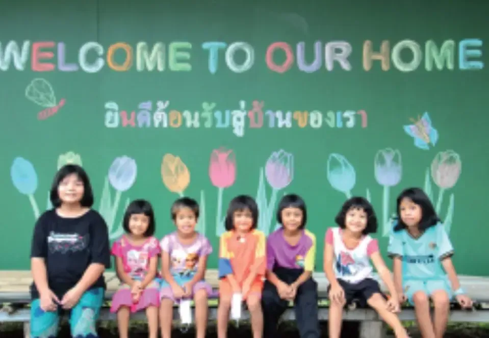 A group of children are sitting in front of a sign that says welcome to our home
