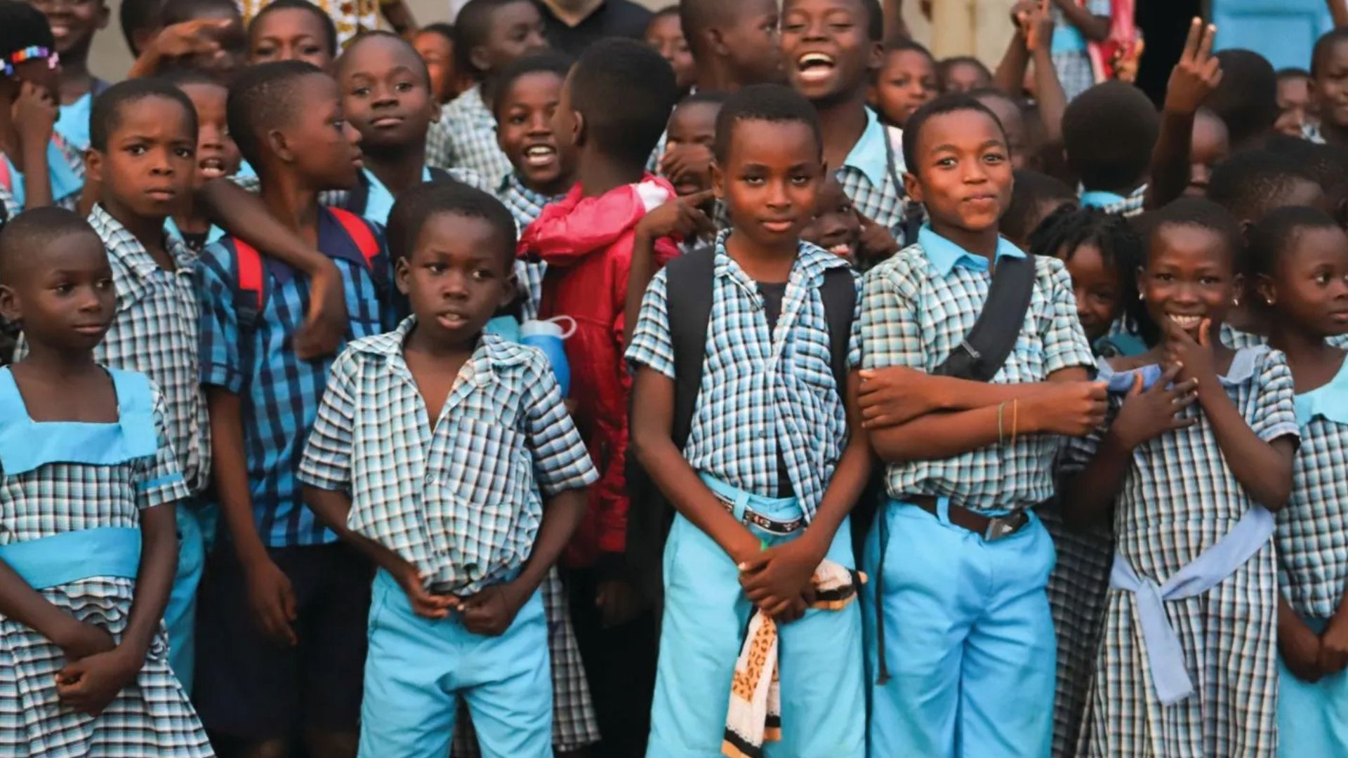 Group of children in school uniforms, mostly smiling and looking at the camera outdoors.