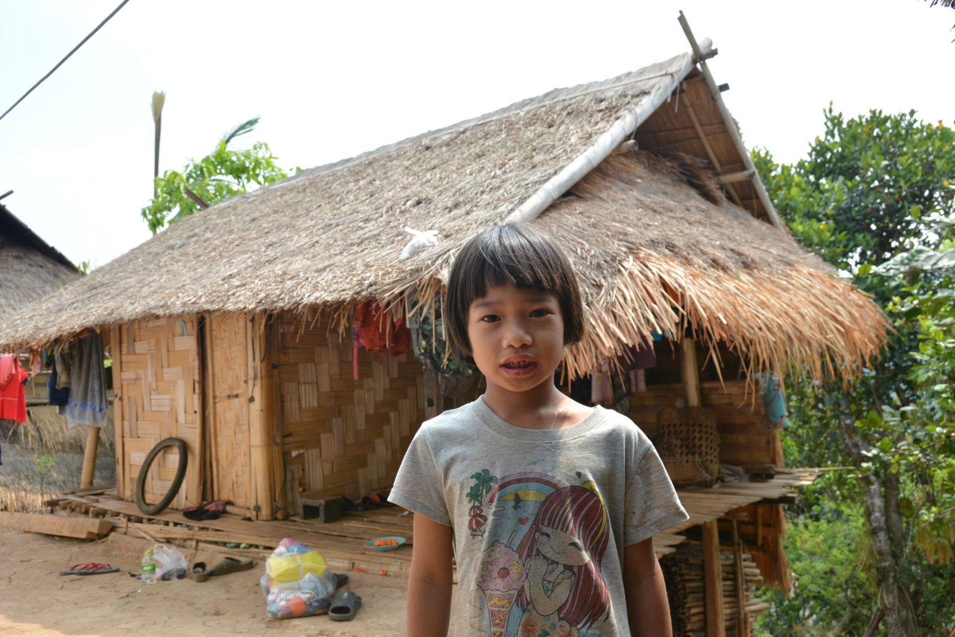 A young girl is standing in front of a thatched hut.