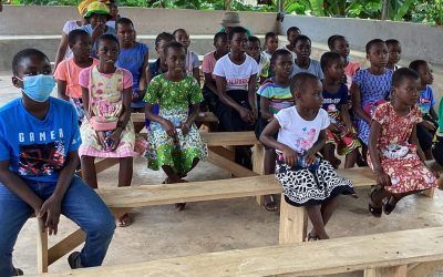 A group of children are sitting on wooden benches wearing masks.