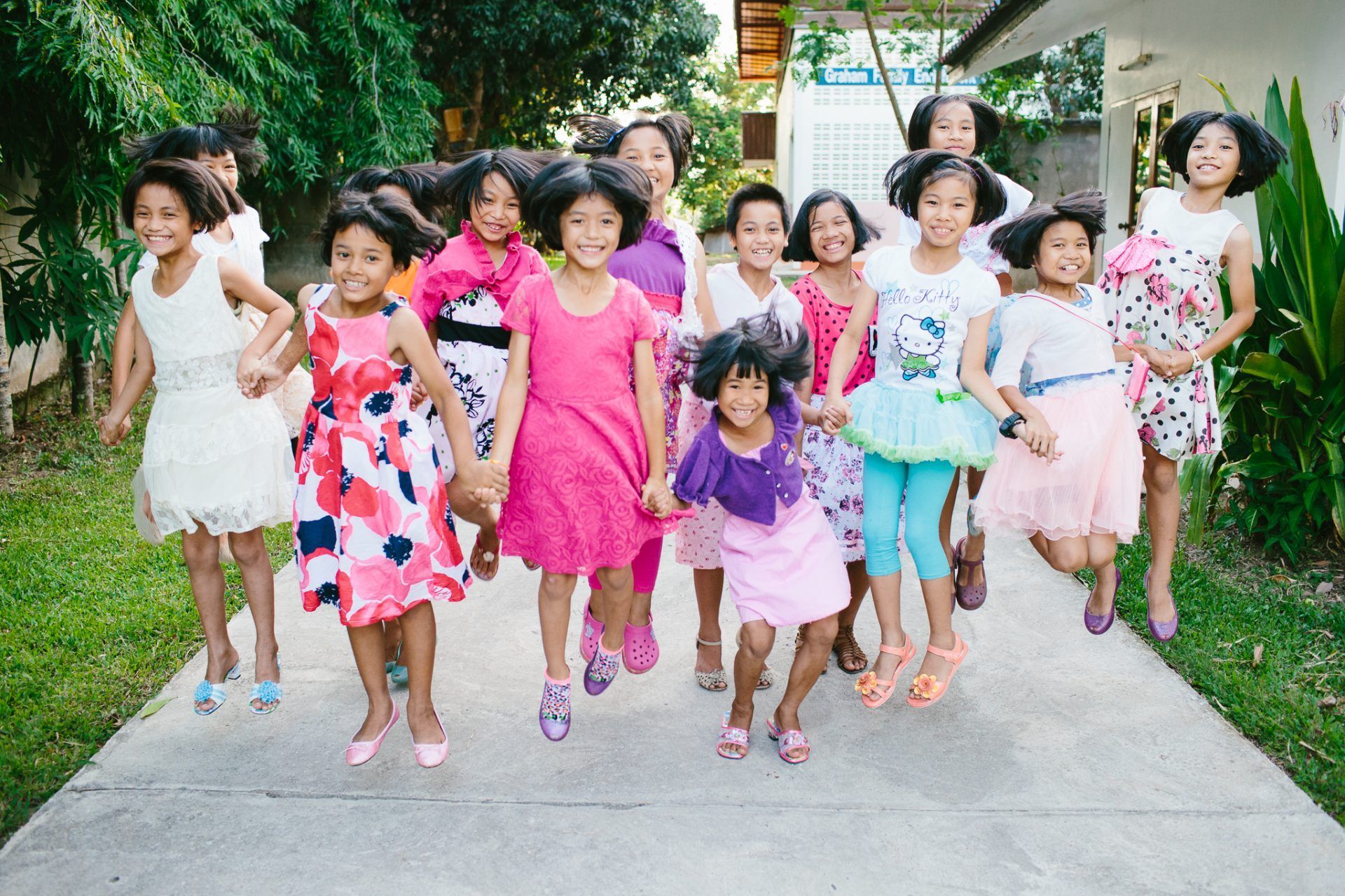 A group of young girls are walking down a sidewalk holding hands.
