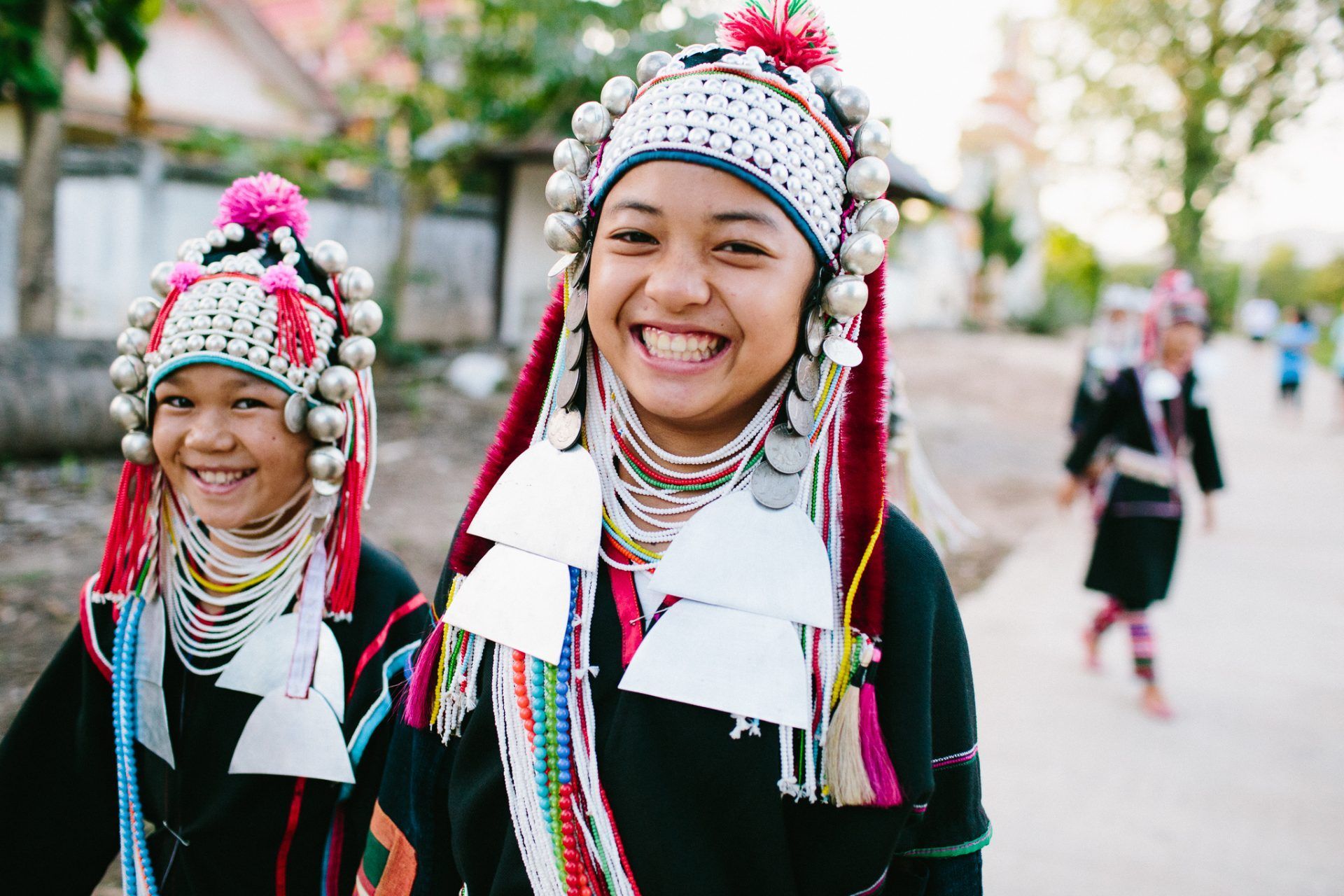 Two young girls wearing traditional clothes and hats are smiling for the camera.