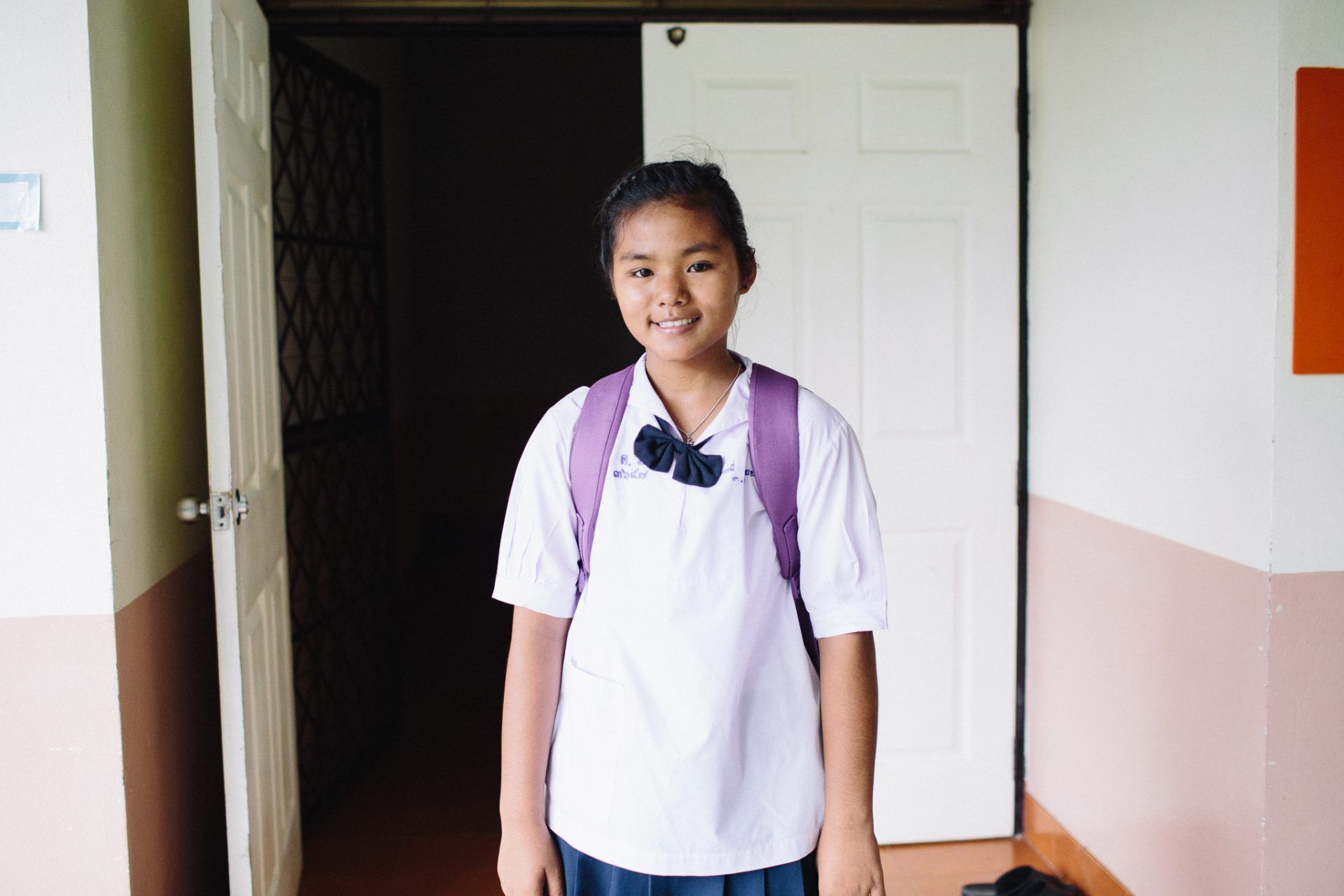 A young girl in a school uniform is standing in front of an open door.