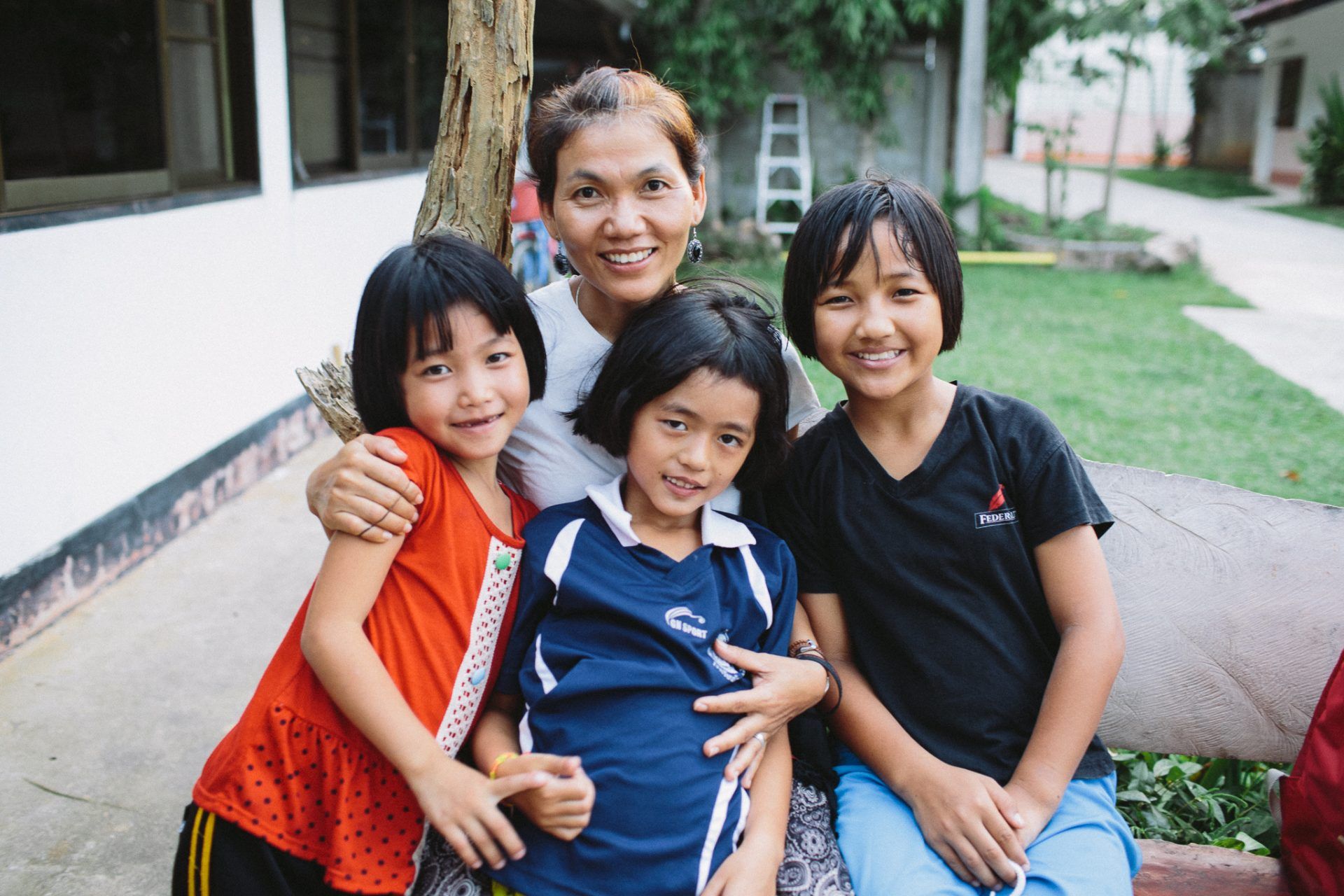 A woman and three children are posing for a picture while sitting on a bench.