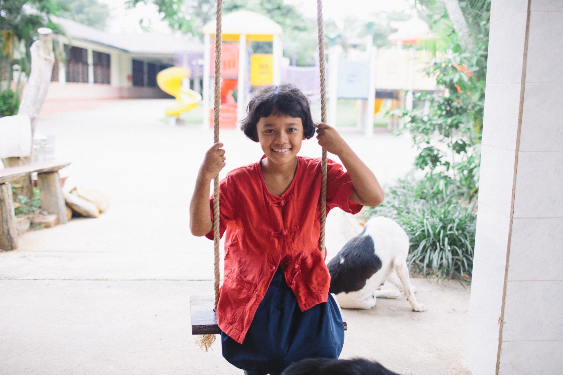 A little girl is sitting on a swing in front of a playground.
