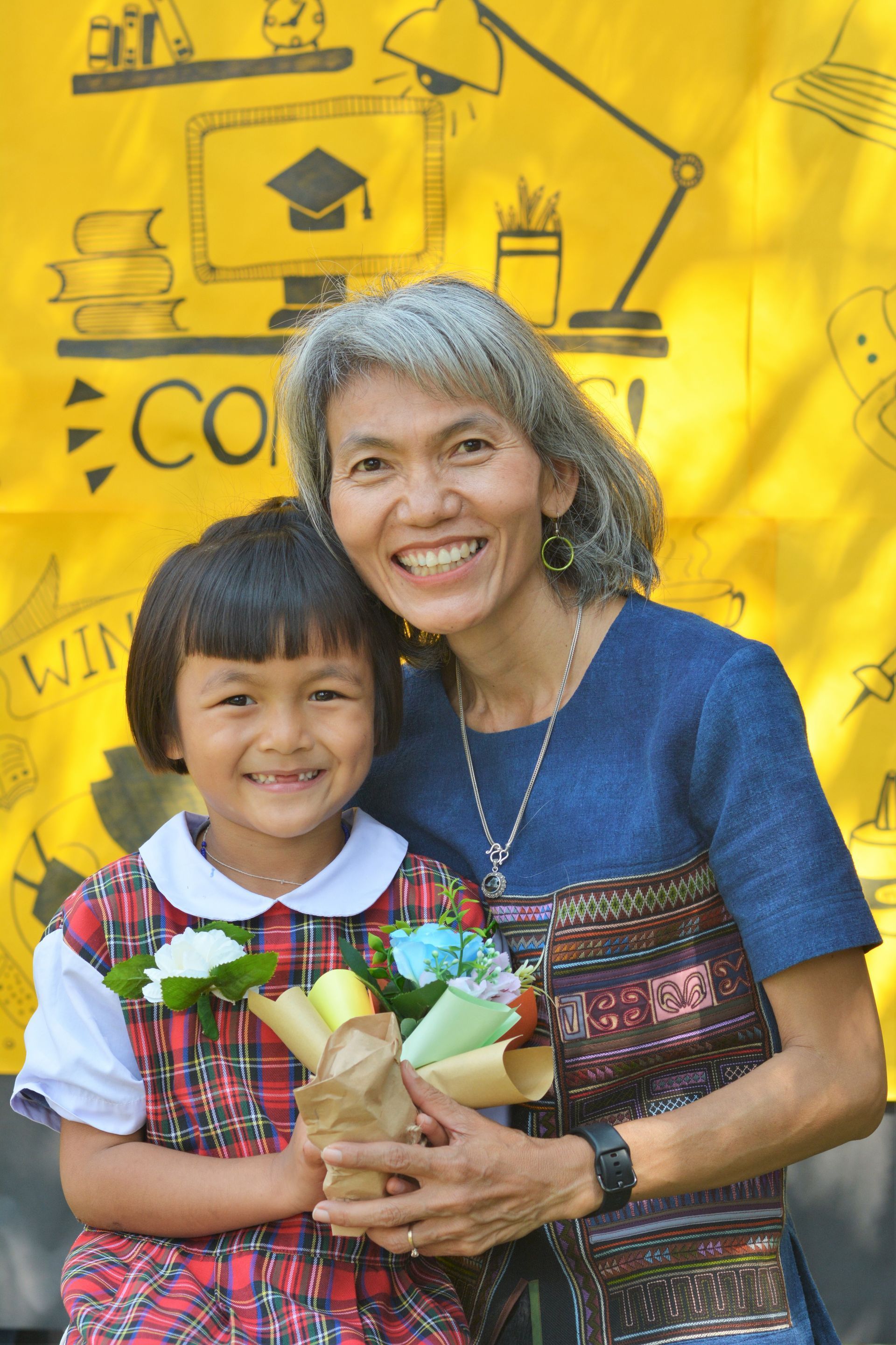 A woman is holding a little girl who is holding a bouquet of flowers.