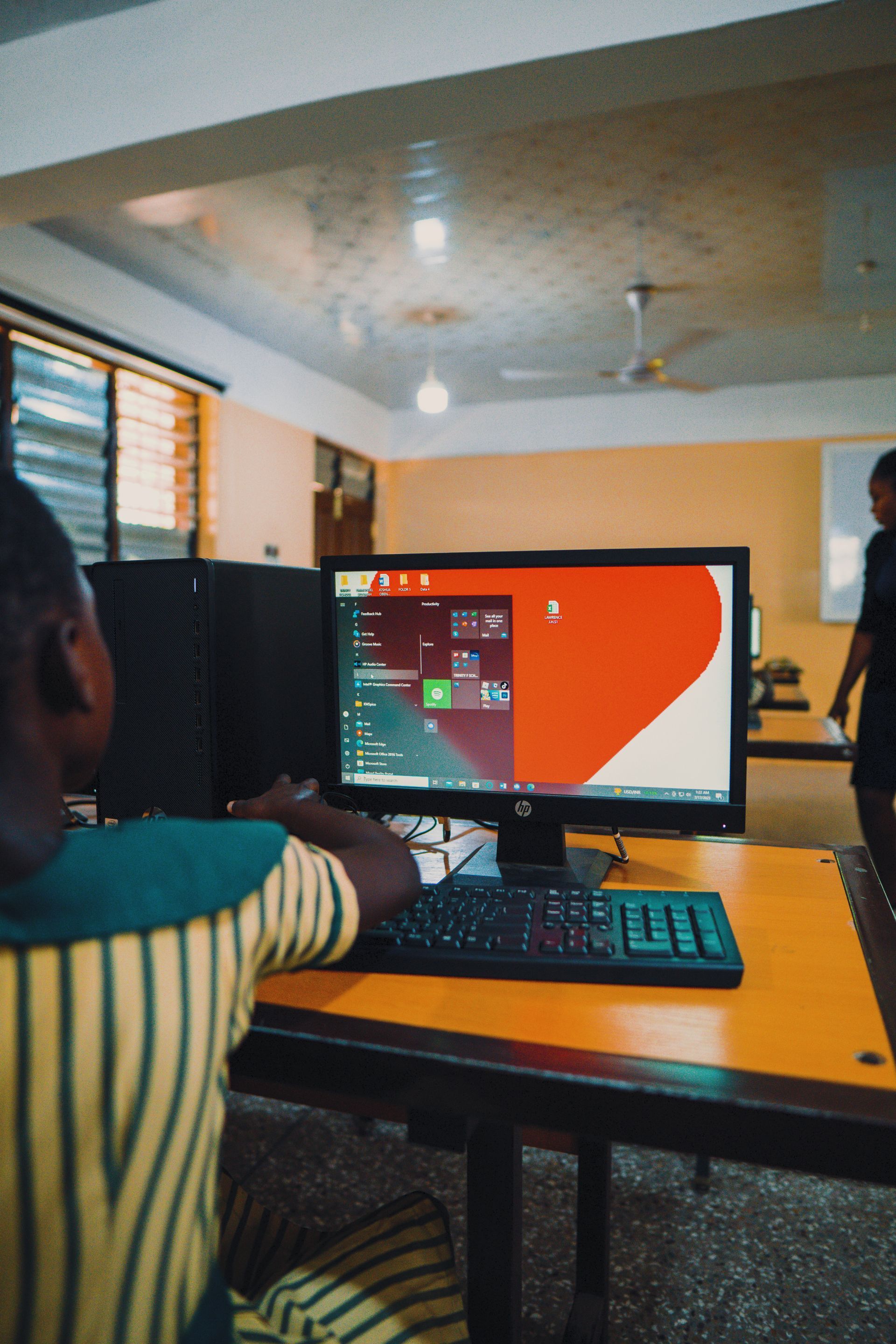 A boy is sitting at a desk in front of a computer monitor.