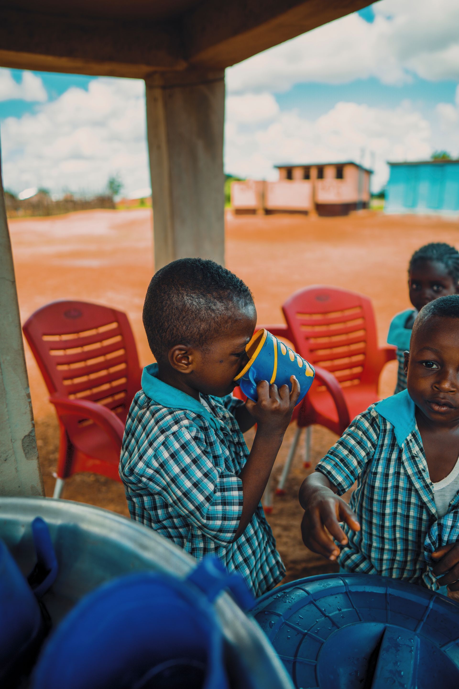 A group of children are drinking water from a bucket.