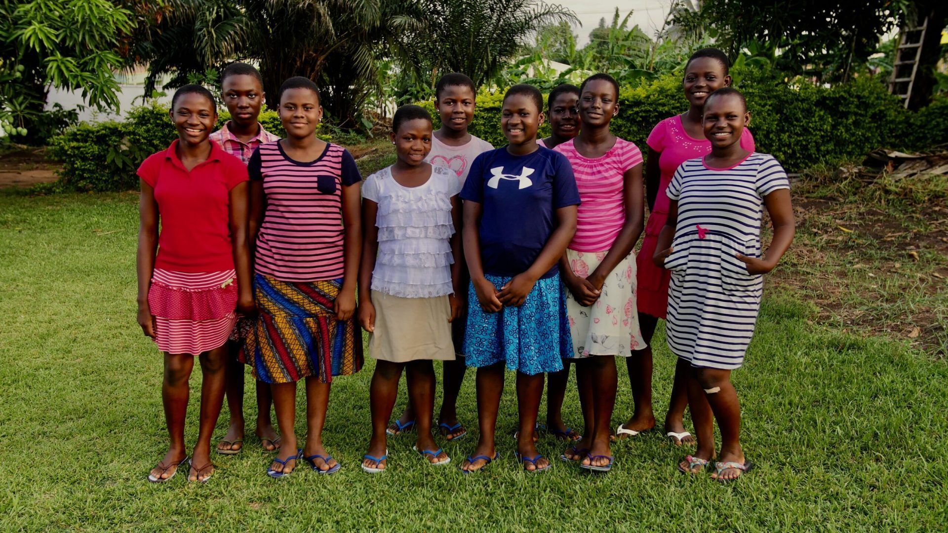 Group of people standing on grass, wearing colorful casual clothing, smiling.