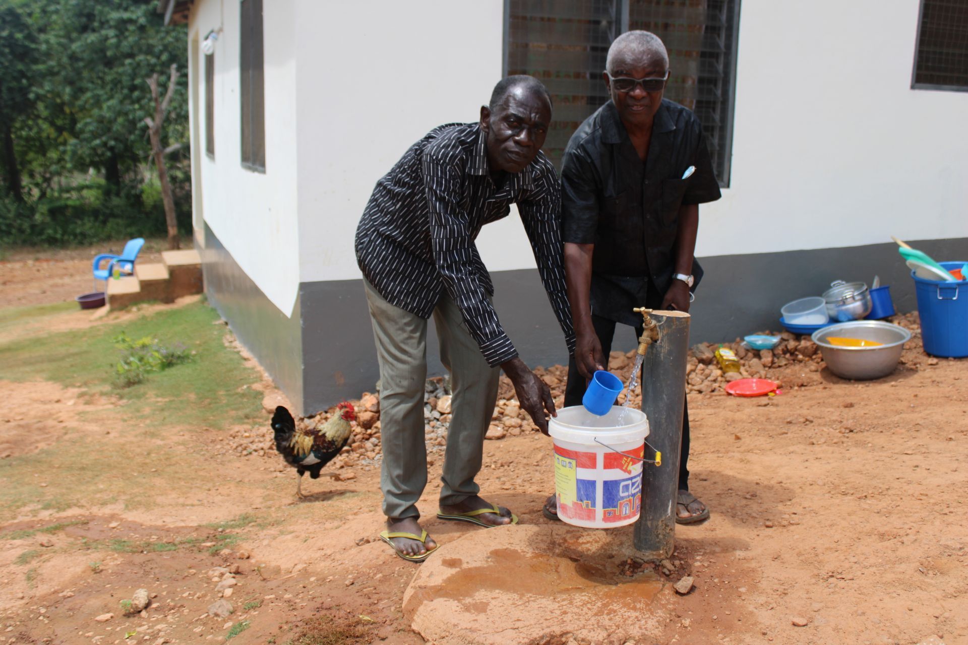 Two men are standing next to each other holding a bucket of water.