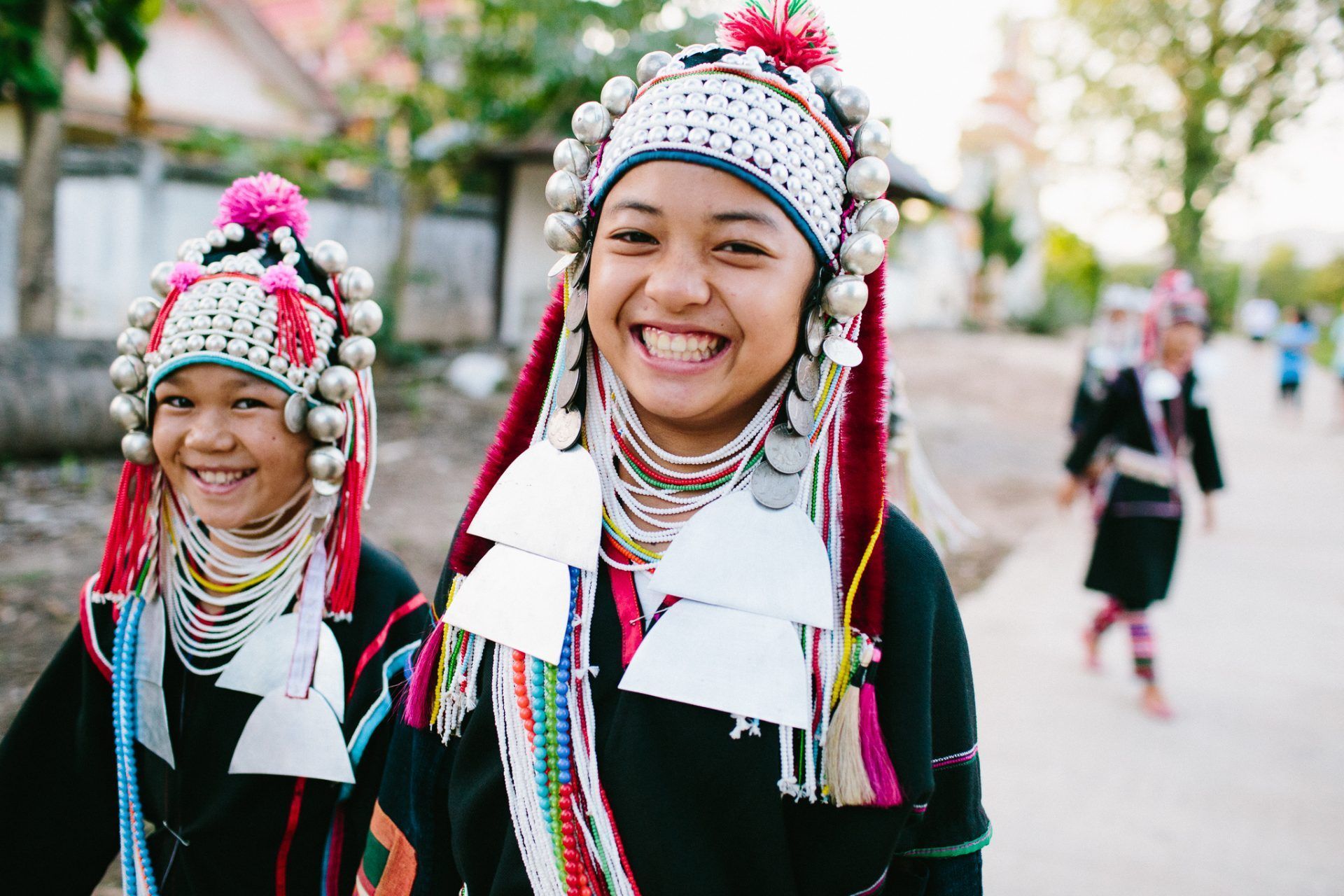 Two smiling people wearing elaborate traditional headdresses and necklaces outdoors.