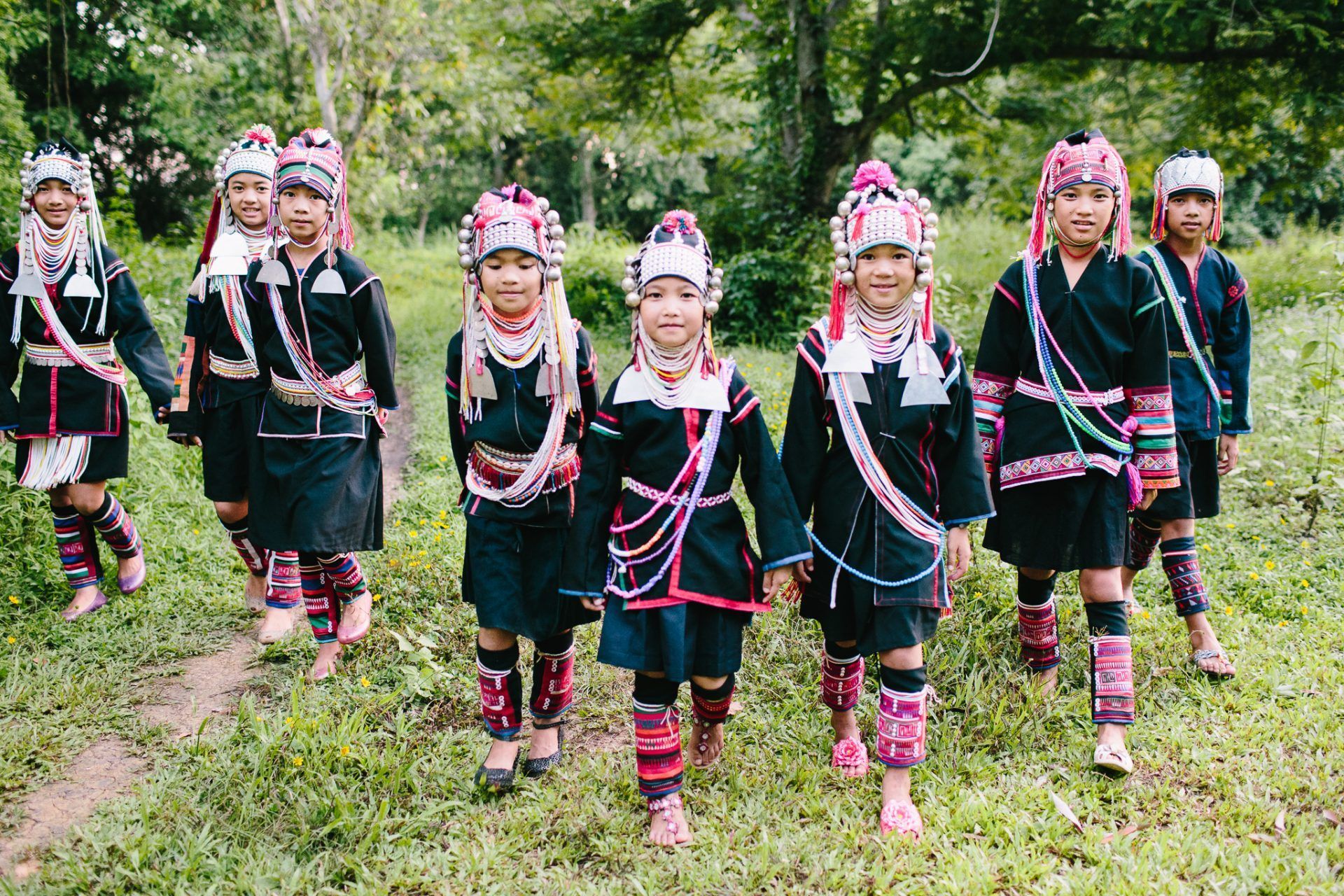 A group of children in traditional costumes are walking through a grassy field.