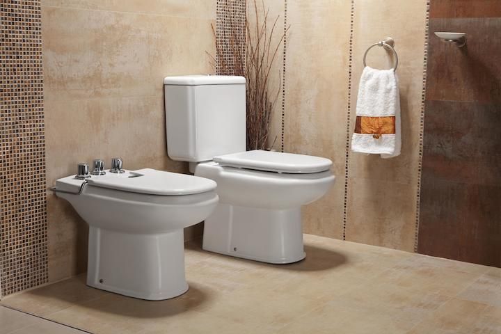 Inodoro y bidet en un baño con paredes en tonos neutros y toalla colgada en una anilla.