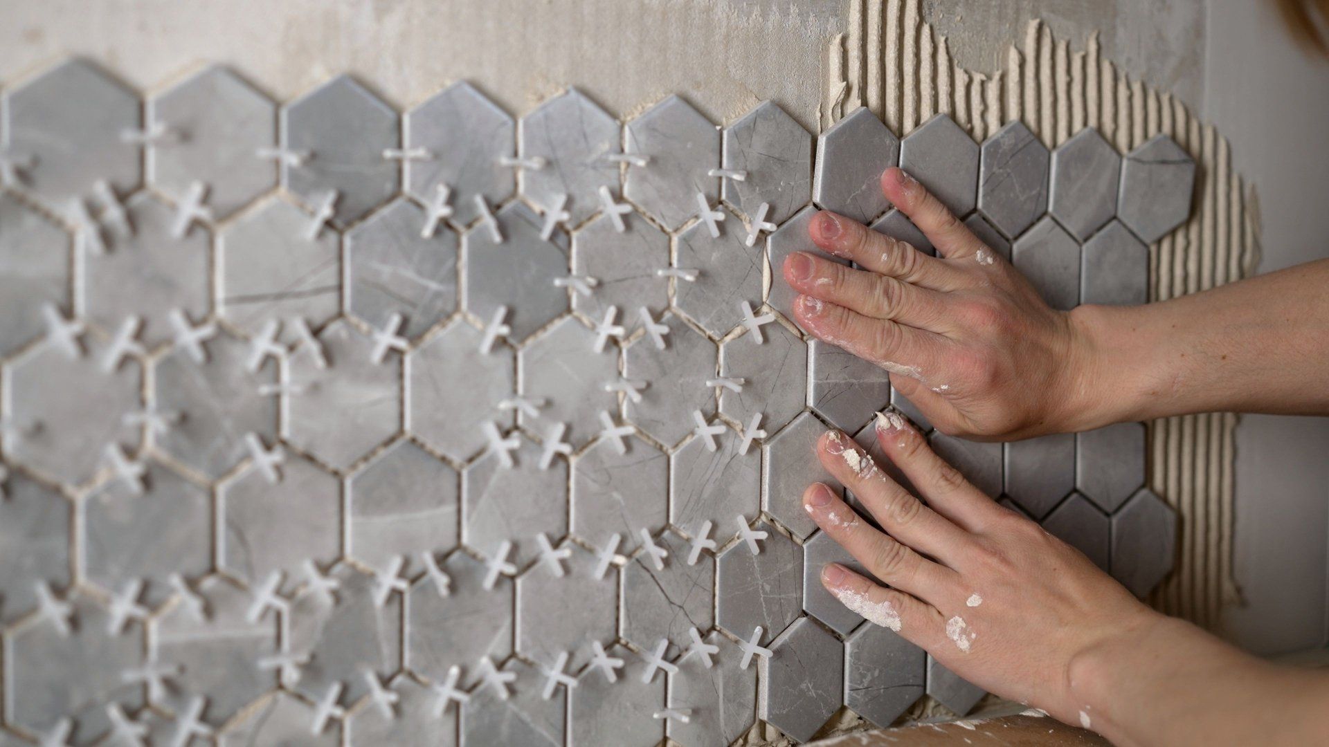 a person is laying tiles on a wall with their hands .
