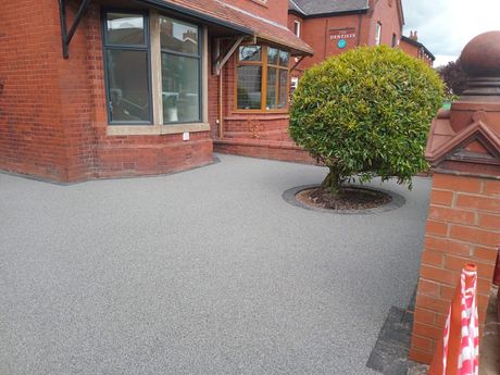 A grey colour resin driveway with a small tree in the centre and a block edging in Cambridge