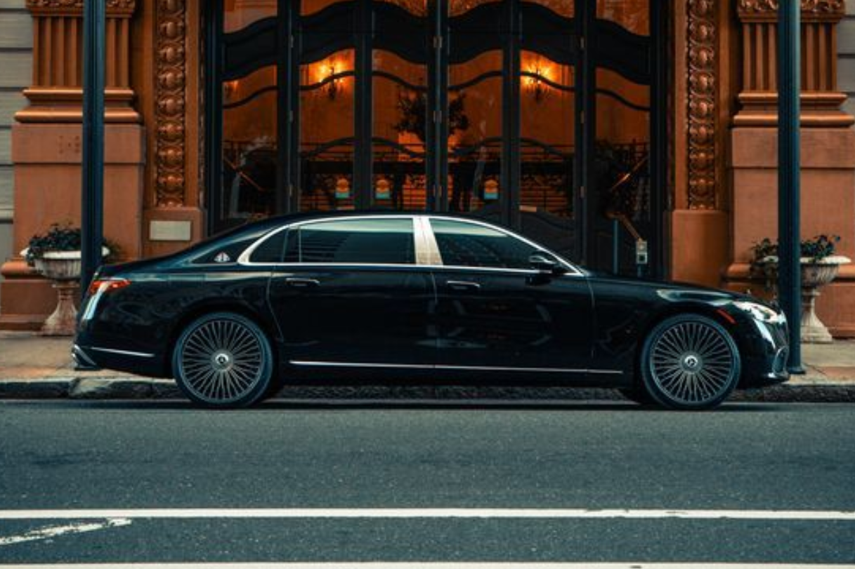 A black Mercedes-Maybach sedan parked on a city street next to a tall grey building and a vibrant red building.