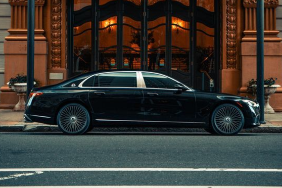 A black Mercedes-Maybach sedan parked on a city street next to a tall grey building and a vibrant red building.