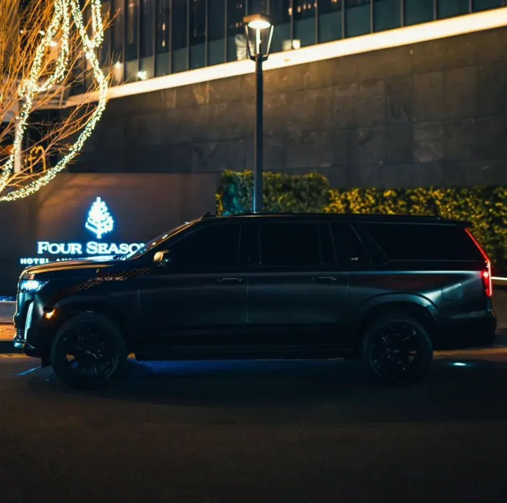 A black SUV parked at night in front of a Four Seasons hotel, illuminated by nearby lights and building signage.