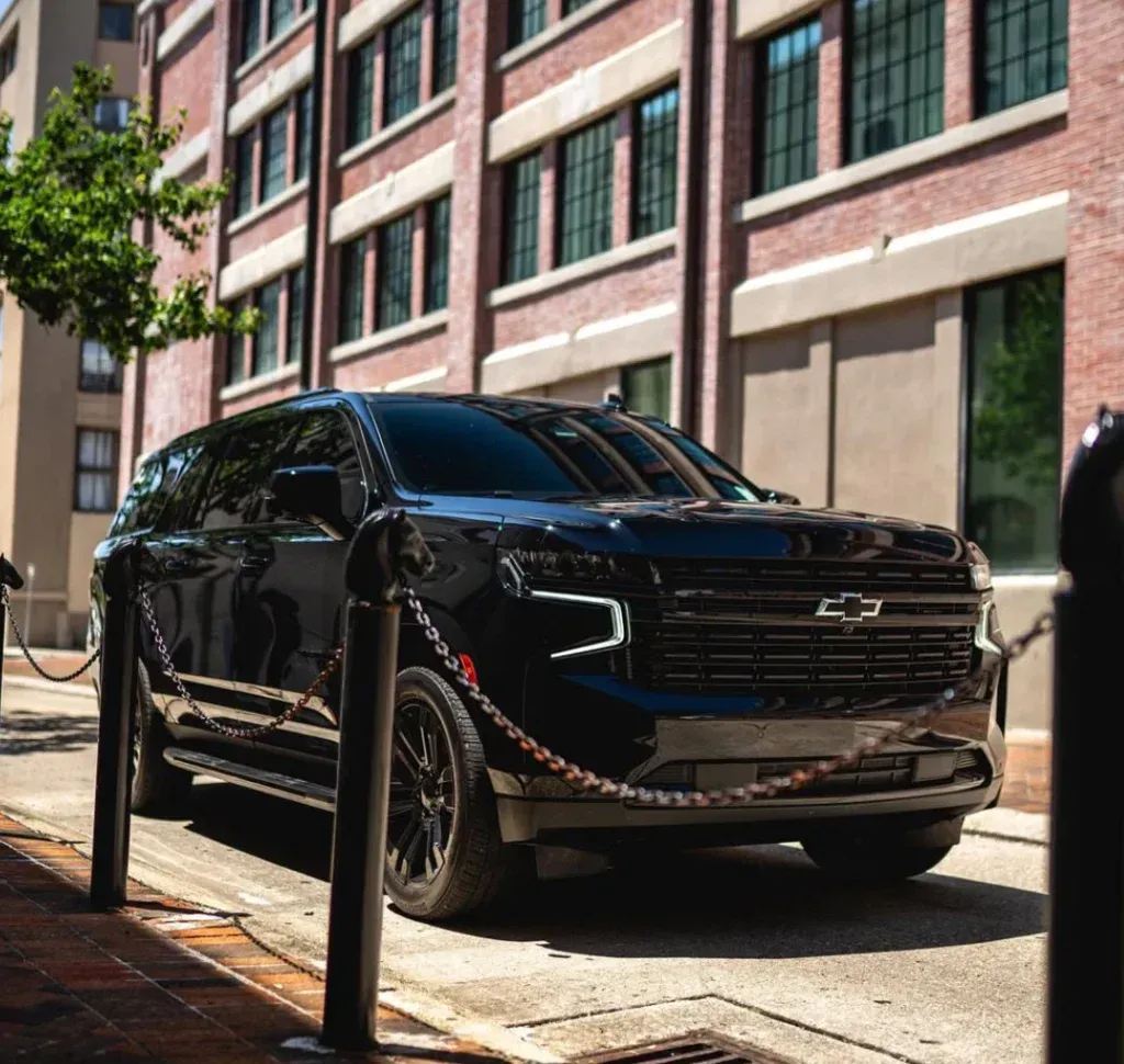 A black Chevrolet SUV is parked on a city street next to a brick building, framed by metal posts and a chain barrier.