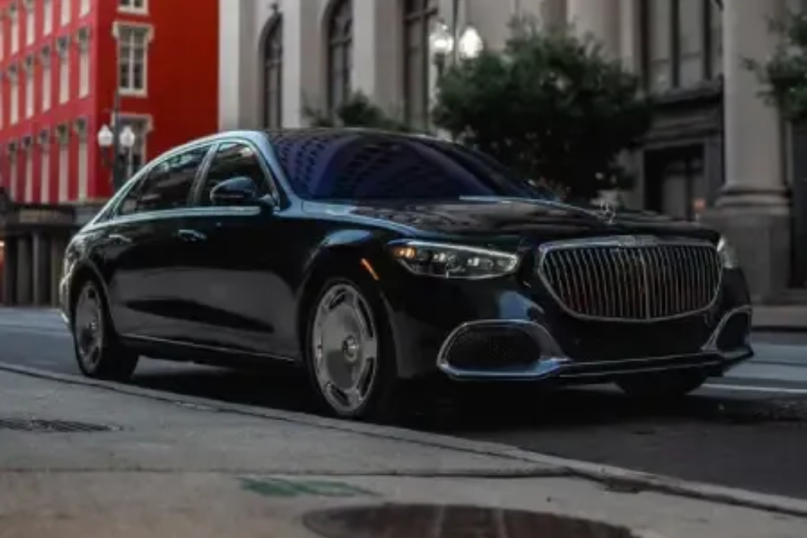A black Mercedes-Maybach sedan parked on a city street next to a tall grey building and a vibrant red building.