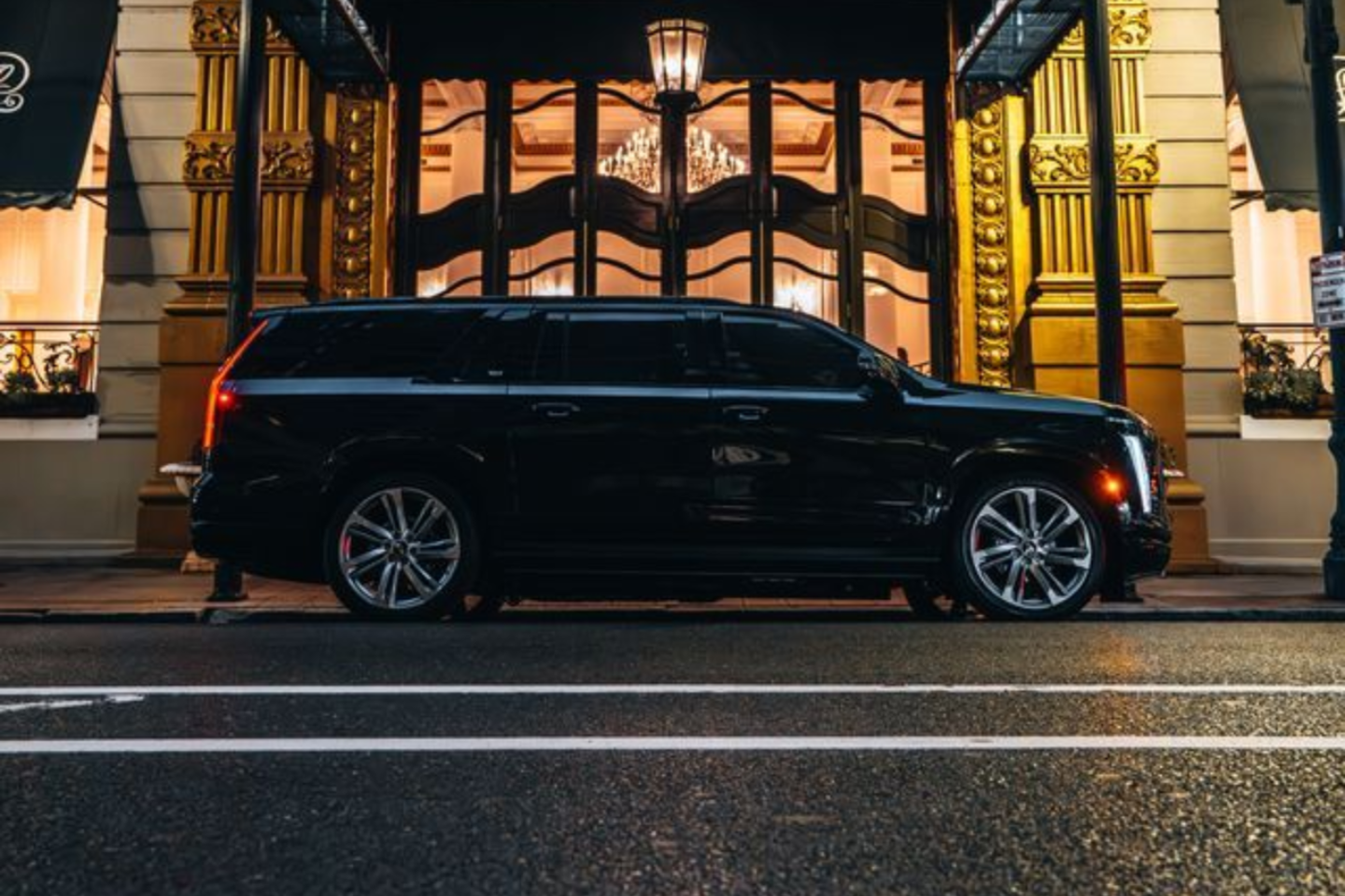 A dark SUV parked on a city street in front of a brick building with many rectangular windows.