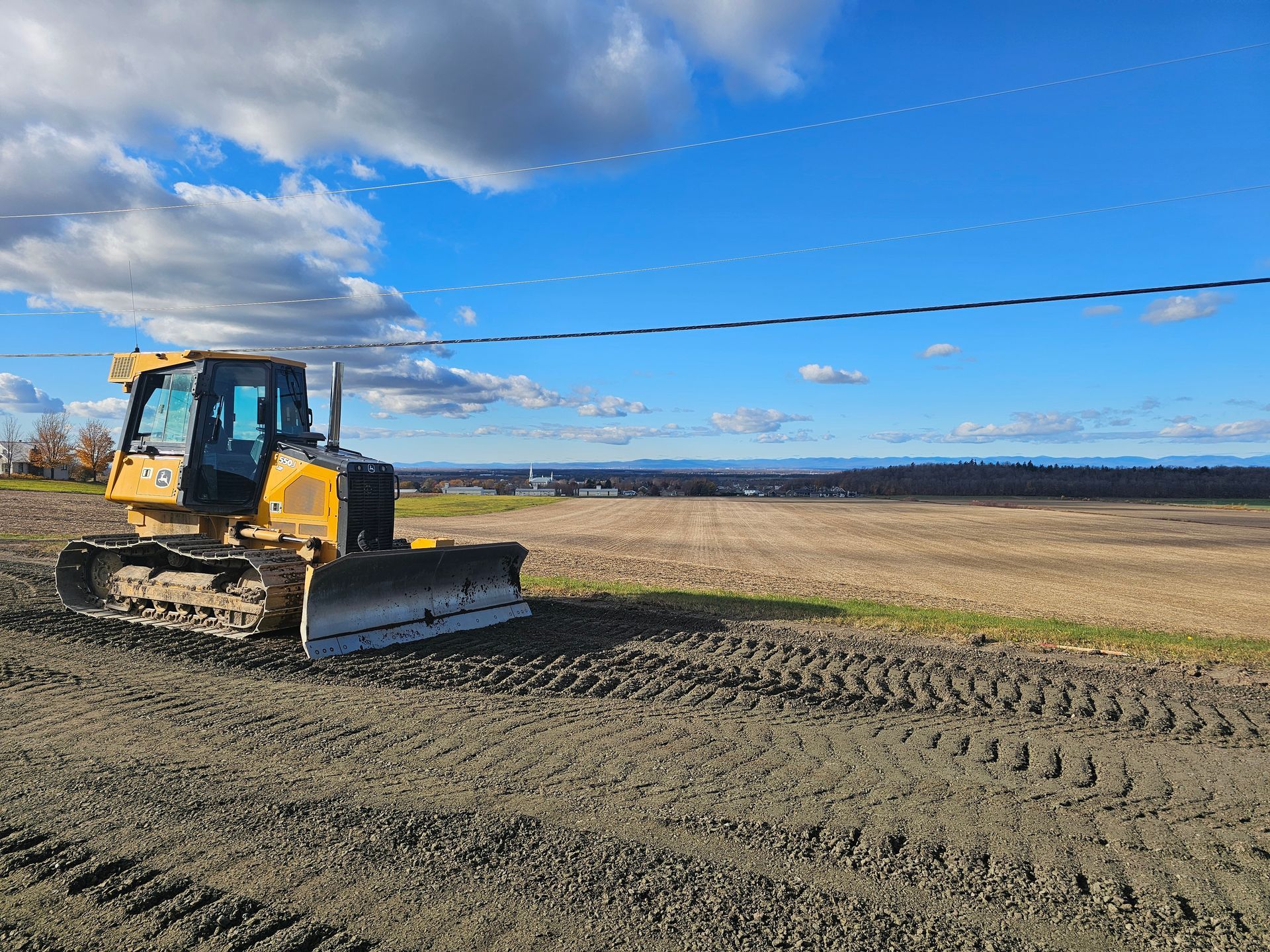 Bulldozer jaune sur un champ de terre sous un ciel bleu nuageux