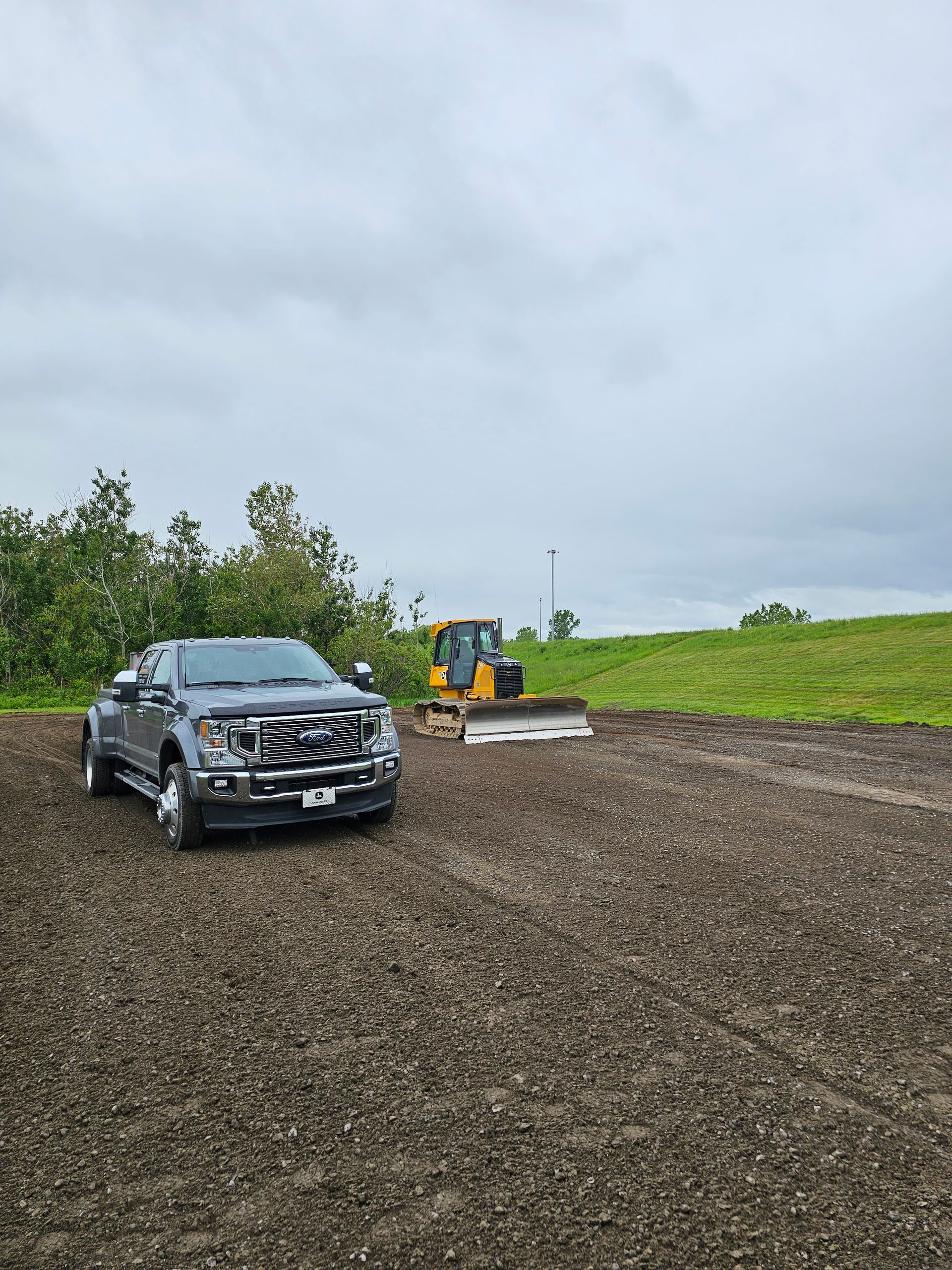 Un SUV noir est garé sur du gravier à côté d'un bulldozer jaune dans un champ rural nuageux.