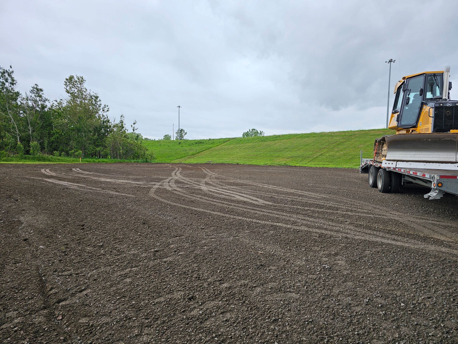 Camion de chantier sur un terrain gravillonné avec une pelle mécanique sur une remorque, colline herbeuse en arrière-plan