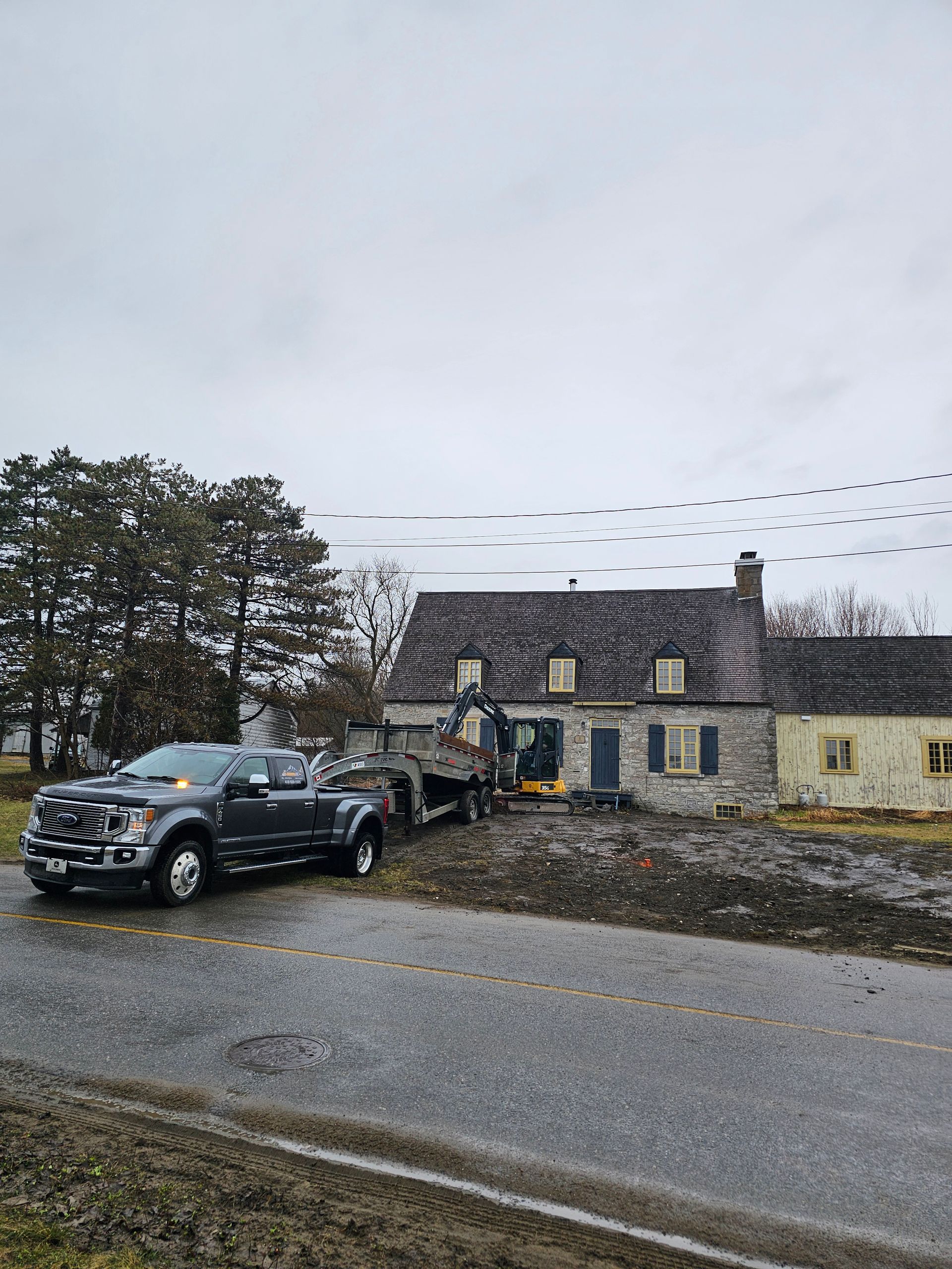Un SUV noir garé devant une maison en pierre sur une route de campagne pluvieuse