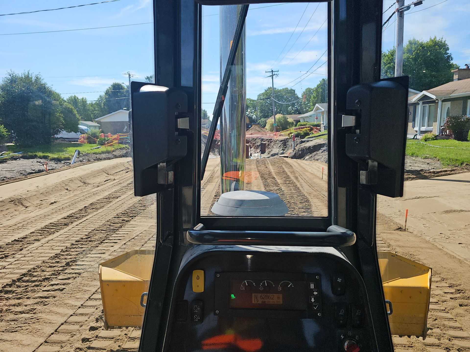 Vue depuis la cabine d'un chariot élévateur sur un chantier boueux avec des tas de terre et des maisons en arrière-plan