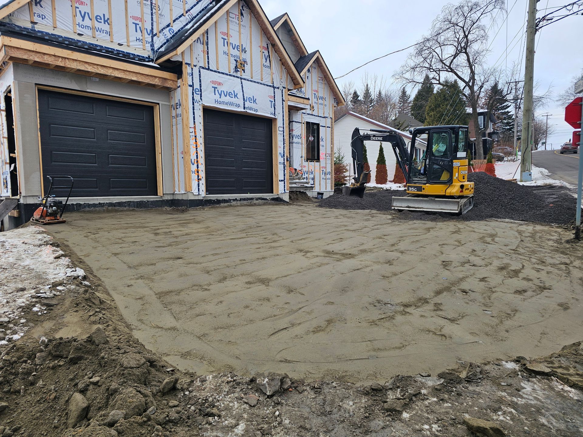 Maison en construction avec allée boueuse en cours de nivellement par une petite excavatrice