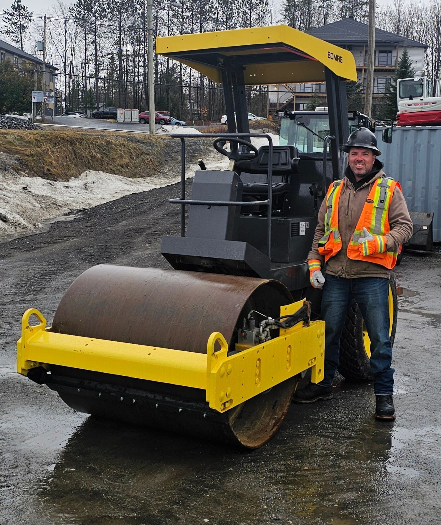 Ouvrier du bâtiment à côté d'un rouleau compresseur jaune sur un chantier humide