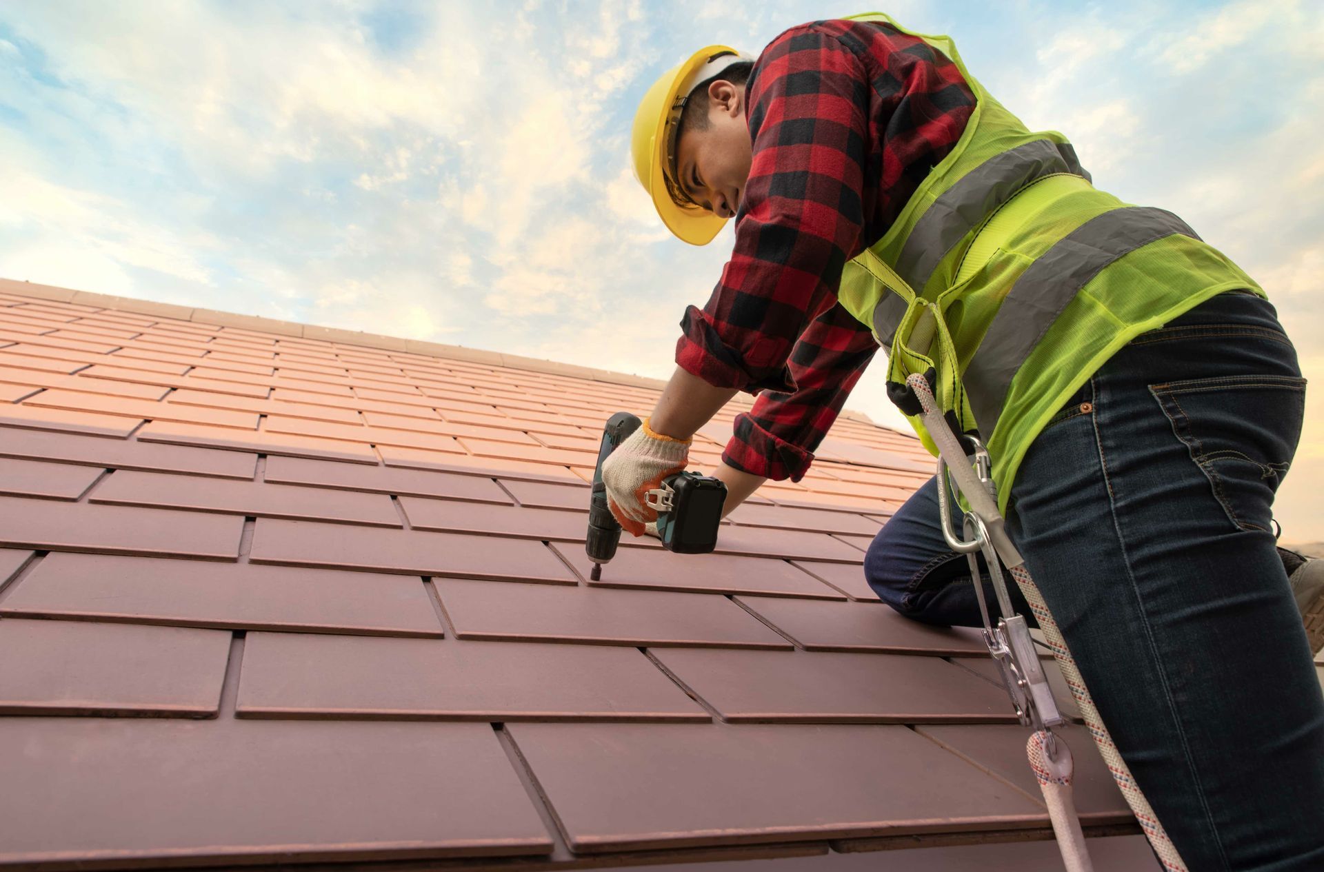 A roofer installs a roof tile with a nail gun.