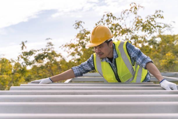 A worker in a hard hat and safety vest installing roofing panels.