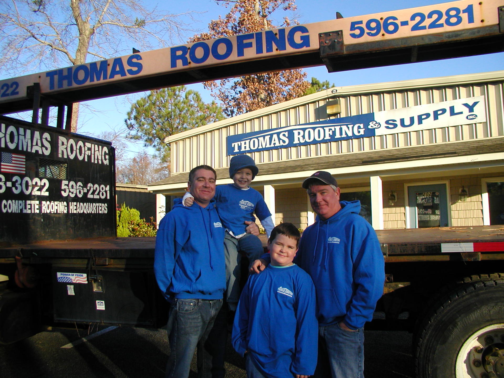 A group of people standing in front of a thomas roofing truck