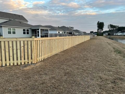 Long wooden fence along a grassy field beside suburban houses under an overcast sky