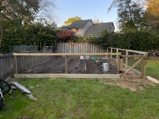 Backyard garden bed with wooden fencing and fresh soil behind a grassy lawn