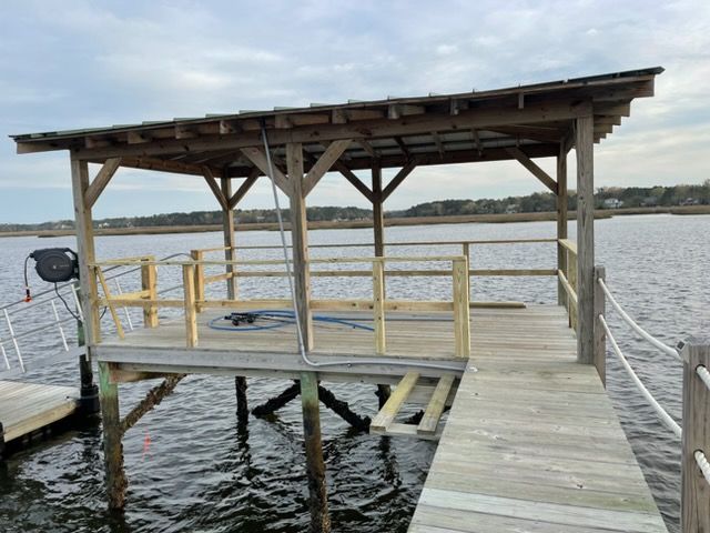 Wooden dock with a covered platform extending over a calm lake under cloudy skies