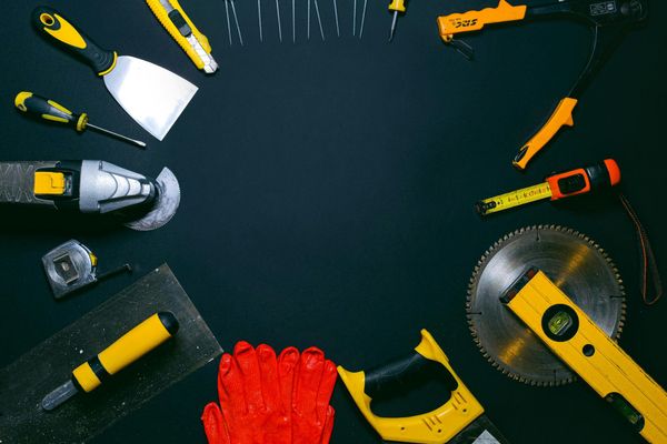 Assorted hand tools arranged in a circular frame on a dark background, with red work gloves at the bottom.